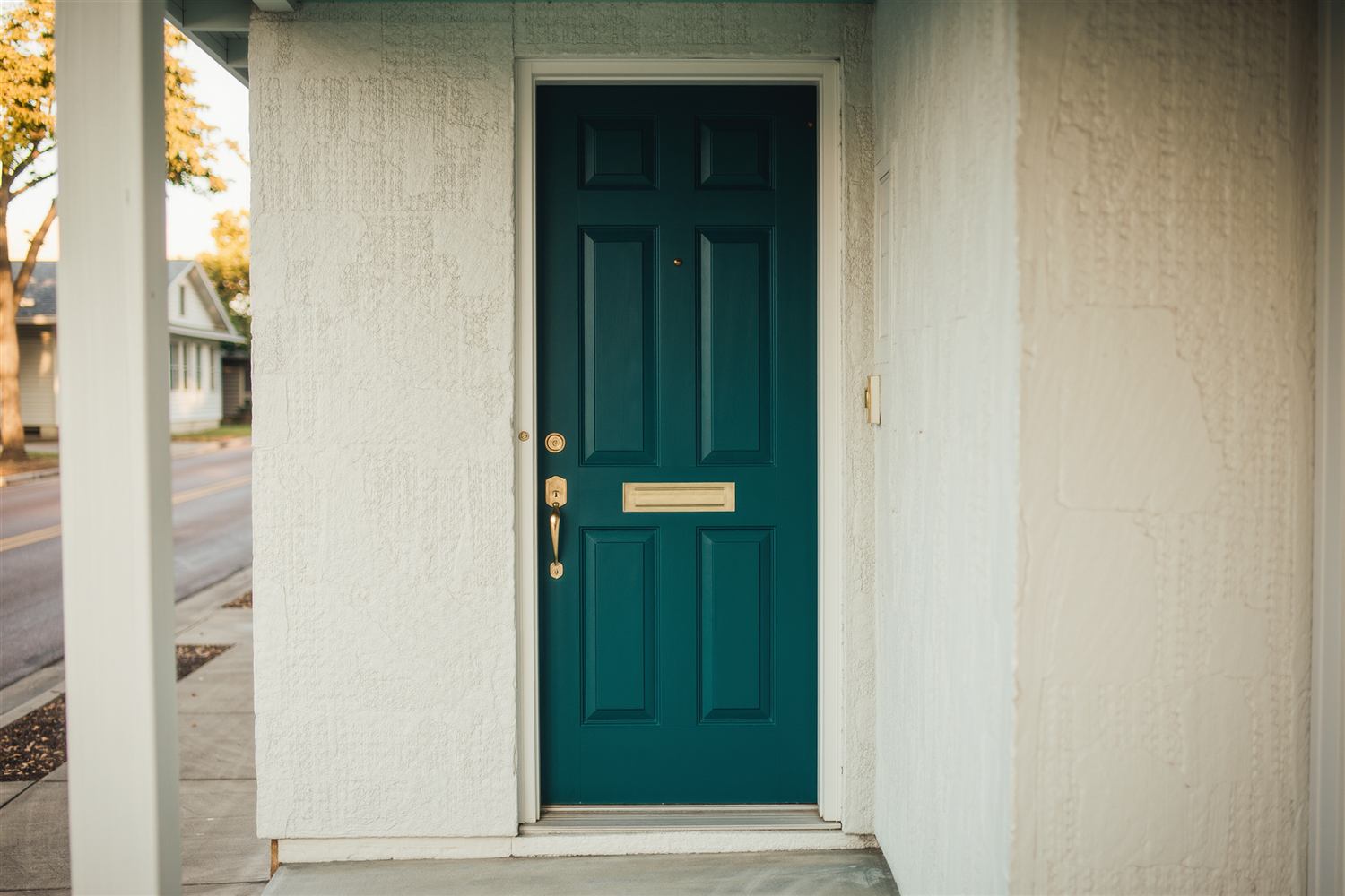 Teal front door with brass hardware set in a stucco wall