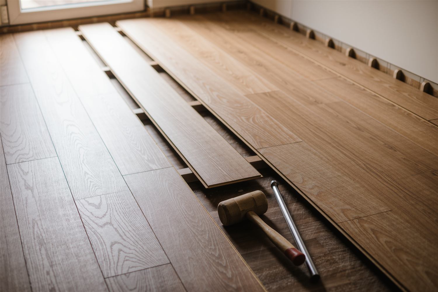 Wide wood planks laid across a room with spacers along the wall and a mallet on the floor